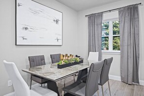 A modern dining room with a marble table, grey upholstered chairs, a black centerpiece, and a large abstract painting on the wall.