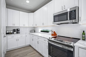 A modern kitchen with white cabinetry, a built-in microwave, a stove, and a coffee maker.