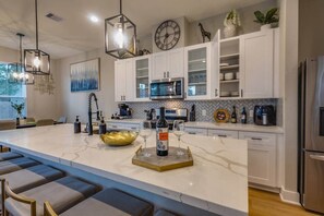 A modern kitchen with white cabinets, a marble island, and stainless steel appliances. - The Houston Haven (Houston)