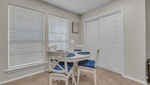 A dining area with a round table and four chairs, two large windows with blinds, a white door, and a framed picture on the wall. - Cozy Retreat Round Rock|Near Dell|Kalahari|Family (Round Rock)