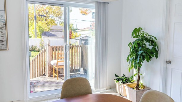 Ein Zimmer mit Holztisch, Stühlen, einem Blumentopf und einer Glastür zum Außenbereich mit Holzlattenzaun und Sitzgelegenheiten.