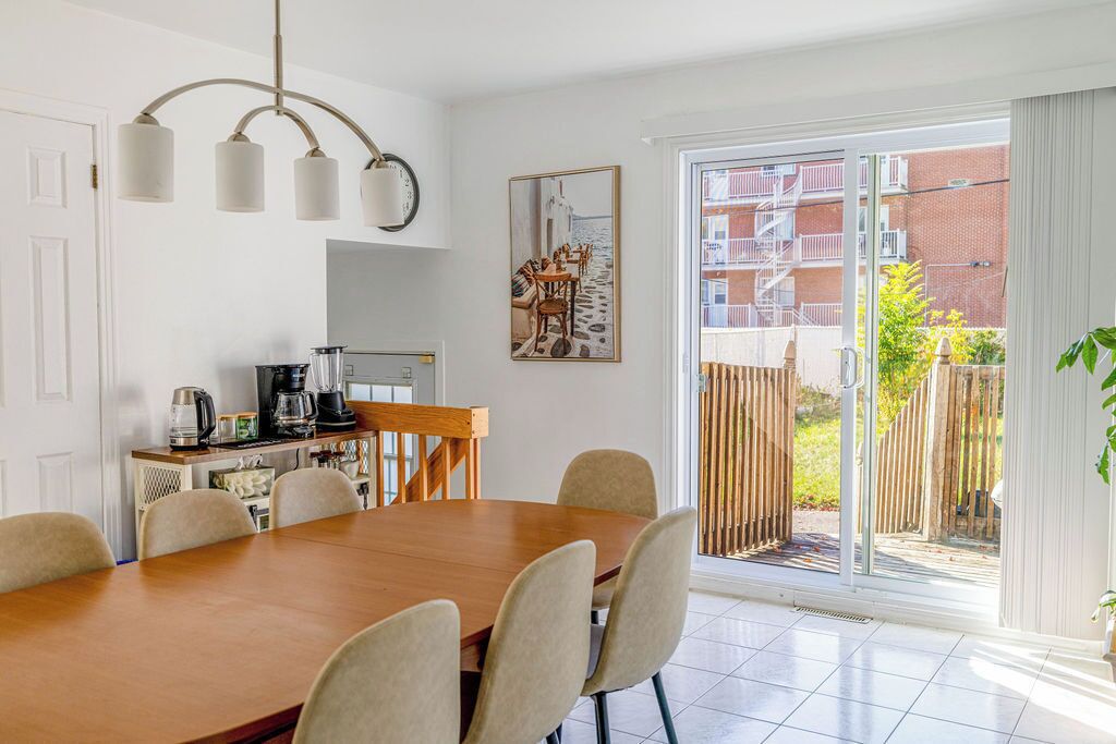 A dining area with a wooden table and chairs, a coffee machine, and a painting on the wall.