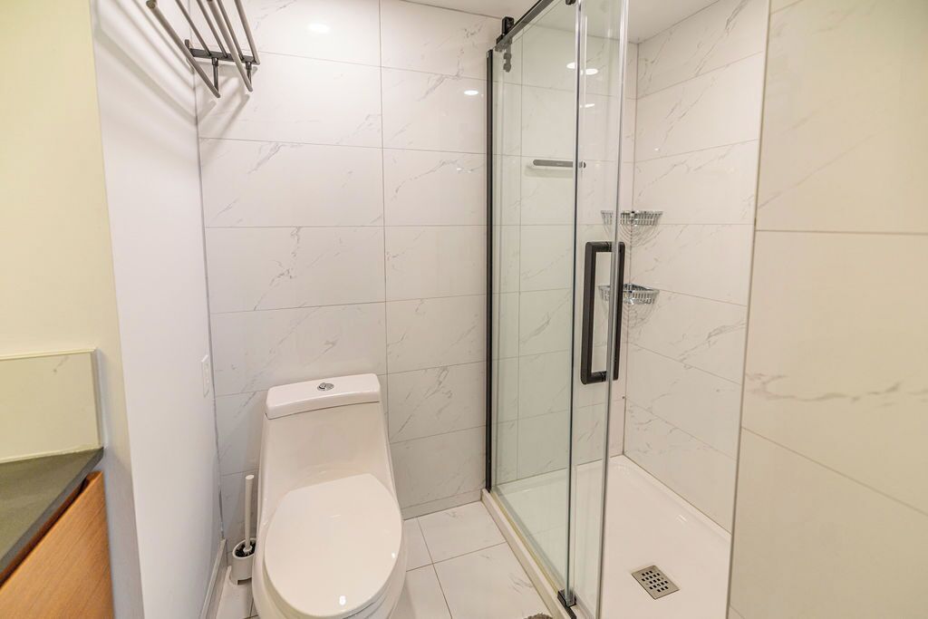 A modern bathroom with a toilet, a glass shower enclosure, and a marble-tiled floor.