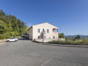 Ein zweistöckiges Gebäude mit einer Treppe, die zu der oberen Etage führt, einem eingezäunten Parkplatz und blauem Himmel.