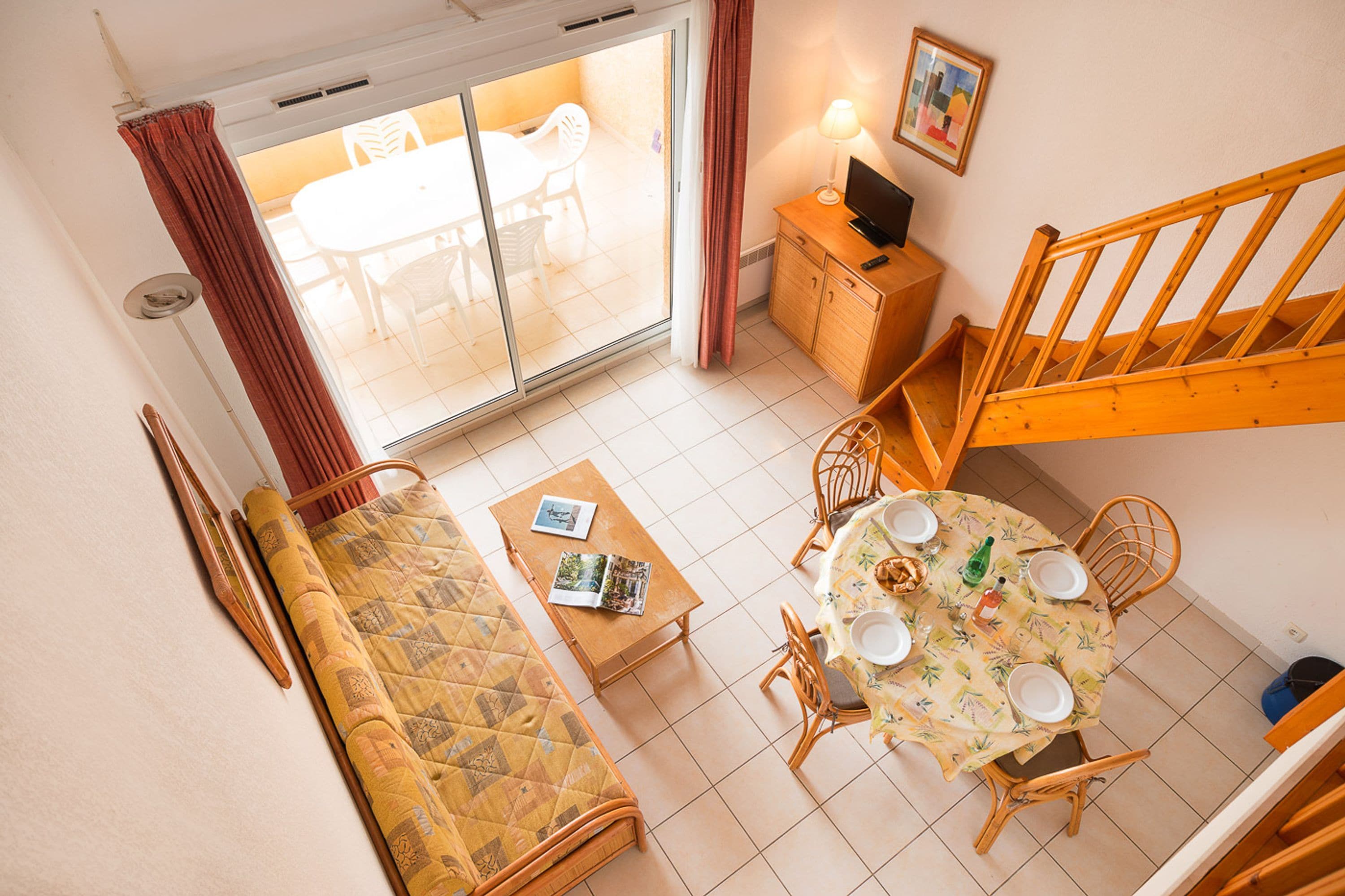 A room with a bed, a dining table with chairs, a sofa, a small cabinet, and a staircase.