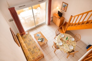 A room with a bed, a dining table with chairs, a sofa, a small cabinet, and a staircase. - R Sidence Alizea Beach 3p6 sea View (Valras-Plage)