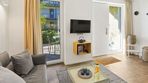 Een moderne woonkamer met een bank, een salontafel met glazen en een fles, een flatscreen-televisie en een glazen schuifdeur die leidt naar een buitenruimte met een tafel en stoelen.