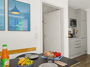 A dining area with a table set for two, a bottle of juice, and a loaf of bread. A kitchen is visible in the background with modern appliances. - Seeblume by Interhome (Lembruch)