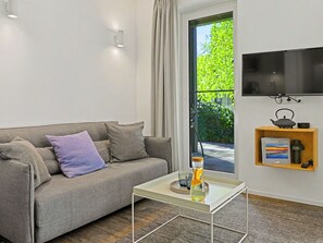 A modern living room with a grey sofa, a glass coffee table, a flat-screen TV mounted on the wall, and a small wooden shelf with a book and a kettle. - Seeblume by Interhome (Lembruch)