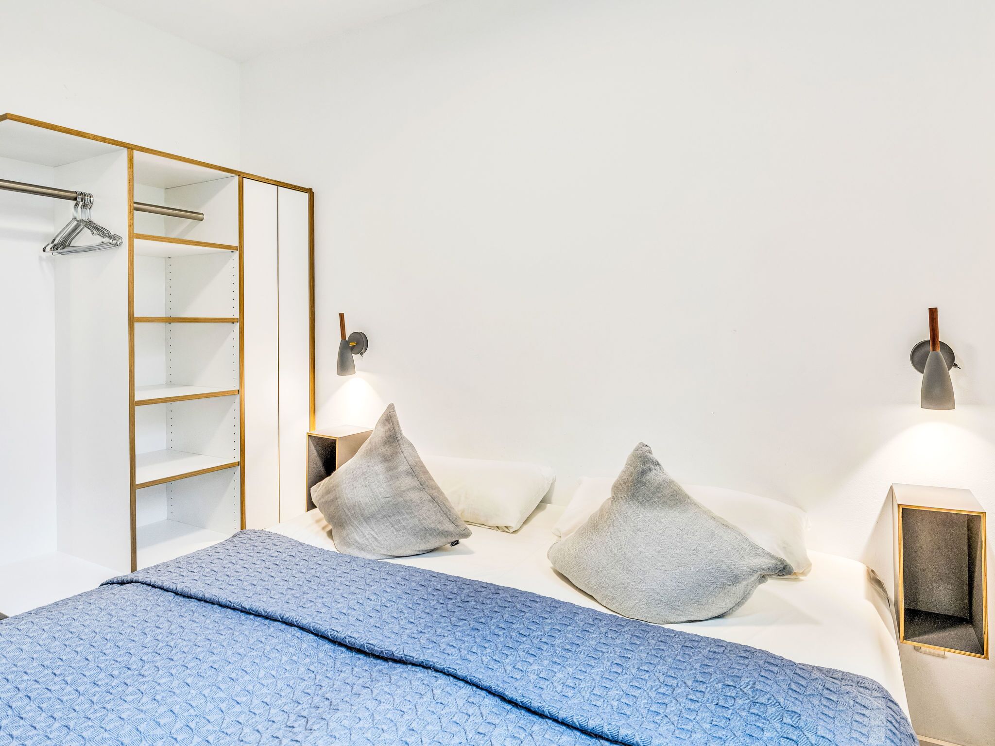 A bedroom with a bed, pillows, a wardrobe, and wall-mounted lights.