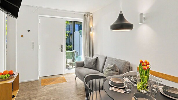 A modern living room with a sofa, dining table set for two, and a television mounted on the wall. - Seewind 601 (Seenähe) by Interhome (Lembruch)