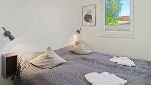 A bedroom with a bed, pillows, a nightstand, a lamp, a framed picture, and a window with a view of greenery. - Seewind 601 (Seenähe) by Interhome (Lembruch)