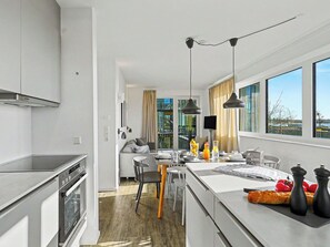 A modern kitchen with a built-in oven, a dining area with a table and chairs, and large windows offering a view. - Seeflair by Interhome (Lembruch)
