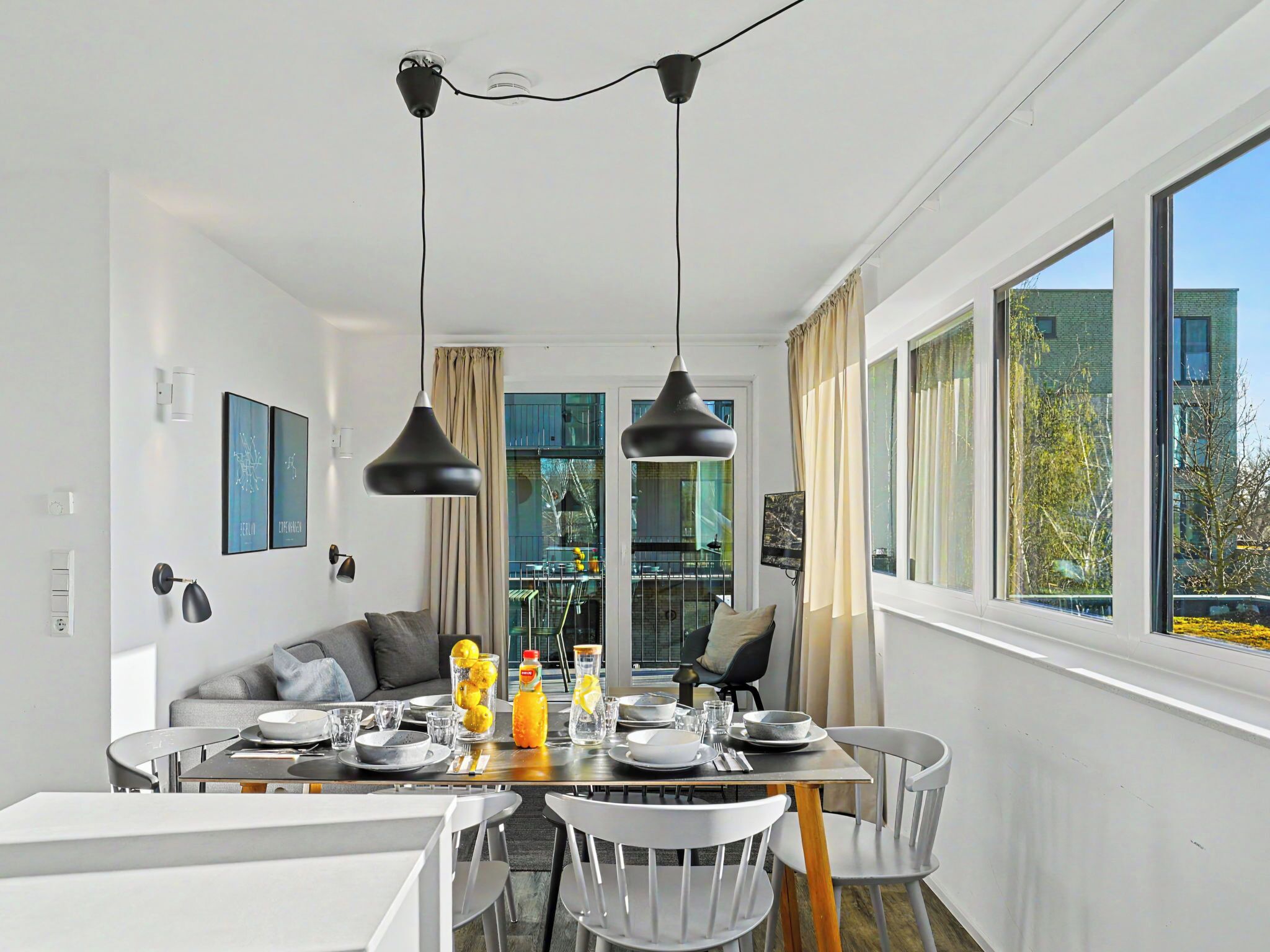 A modern dining area with a glass table, white chairs, and black pendant lights.