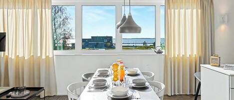 A dining area with a table set for four, a view of the sea through large windows, and a modern pendant light.