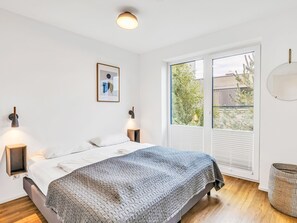 A bedroom with a bed, two wall-mounted lamps, a framed picture, a window with blinds, and a wicker basket. - Seegold 638 (Seenähe) by Interhome (Lembruch)