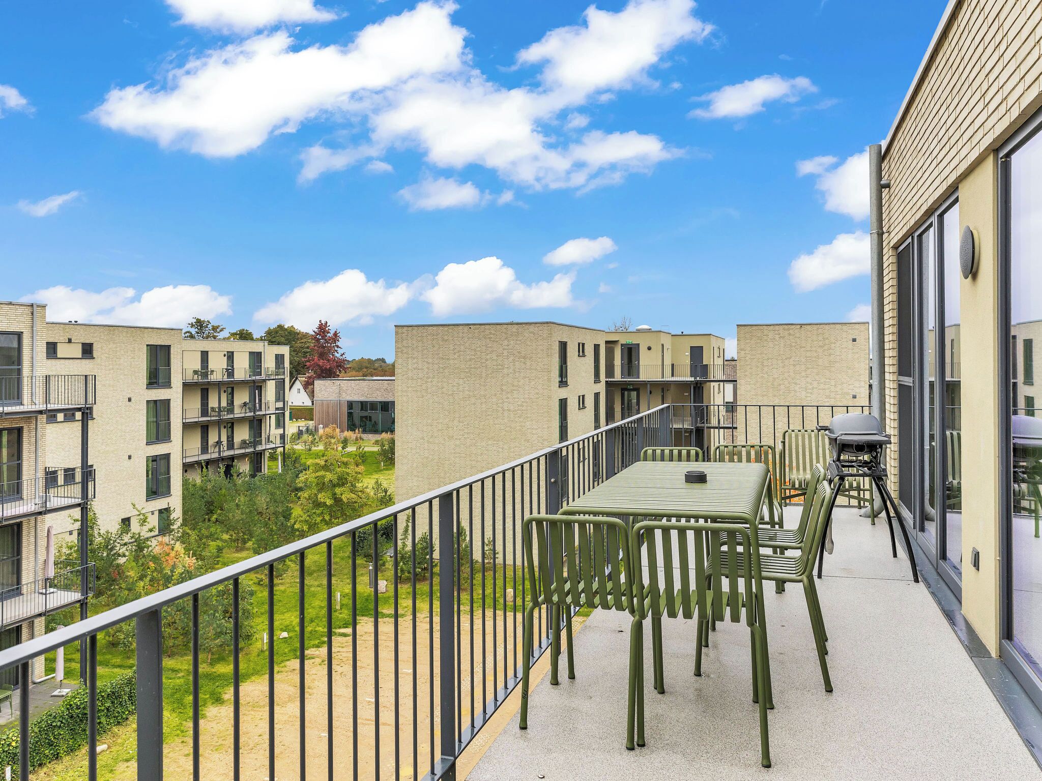 Een balkon met een tafel en stoelen, met uitzicht op een woonwijk met moderne gebouwen.