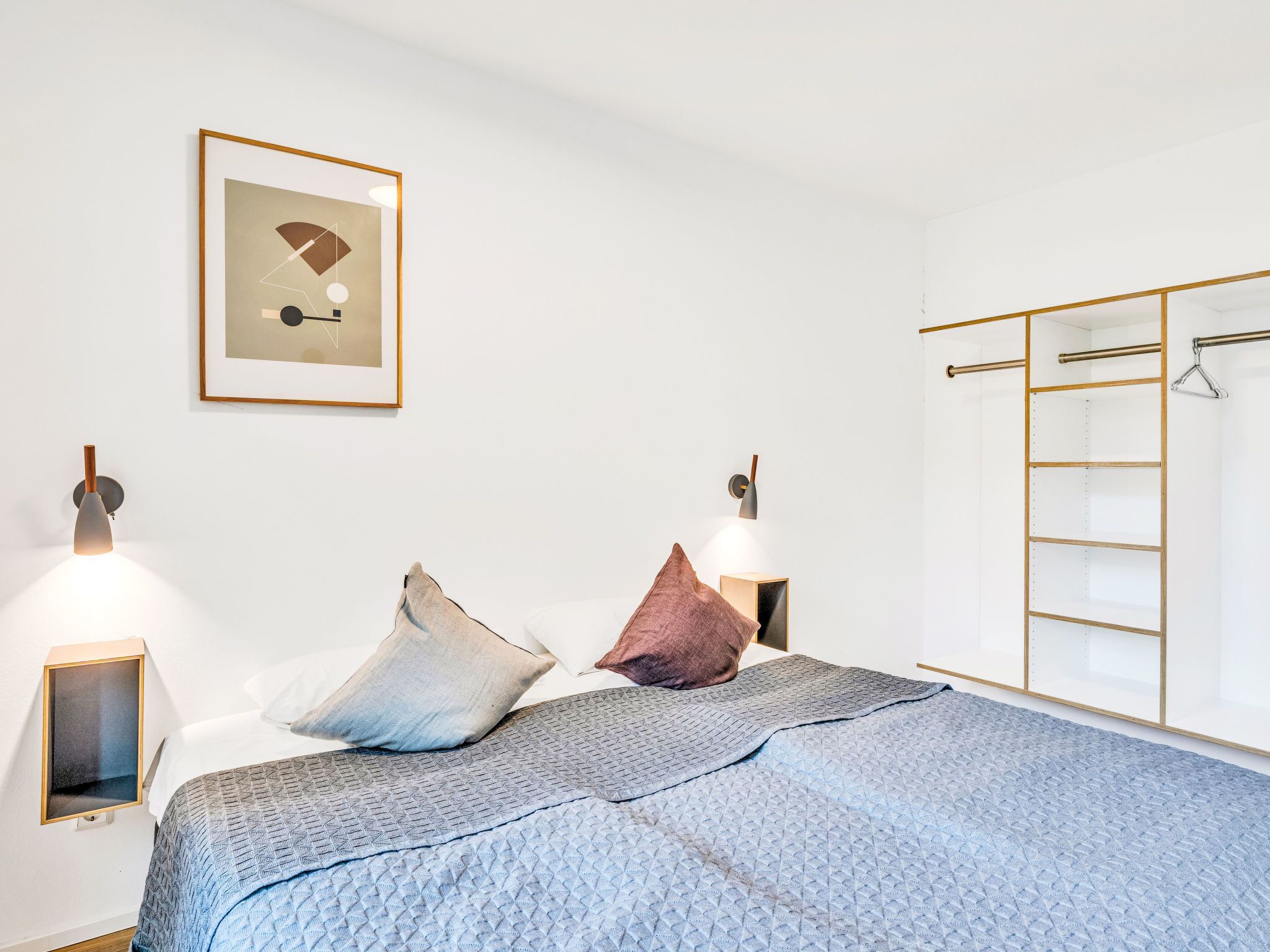Quarto com cama, almofadas, abajures, um quadro emoldurado e um guarda-roupa.