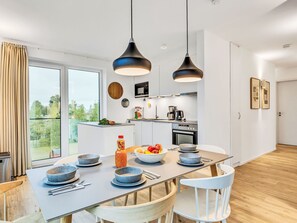 Une cuisine moderne dotée d’un îlot central, de luminaires suspendus et offrant une vue sur l’extérieur.