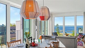 A dining area with a table set for four, large windows with a view of the sea, and a balcony with outdoor seating.
