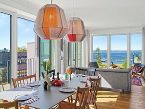 A dining area with a table set for four, large windows with a view of the sea, and a balcony with outdoor seating. - Penthouse Seevibes by Interhome (Lembruch)