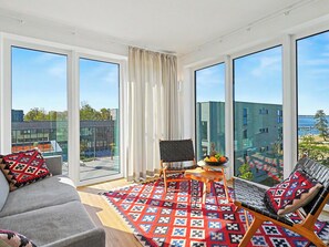 A modern living room with a sofa, a chair, a small table with fruit, and large windows offering a city view. - Penthouse Seevibes by Interhome (Lembruch)