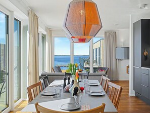 A dining area with a view of the sea, a modern pendant light, and a kitchen with a flat-screen TV. - Penthouse Seevibes by Interhome (Lembruch)