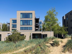 Un edificio moderno de varios pisos con amplios ventanales y balcones, rodeado de vegetación natural y un cielo despejado.