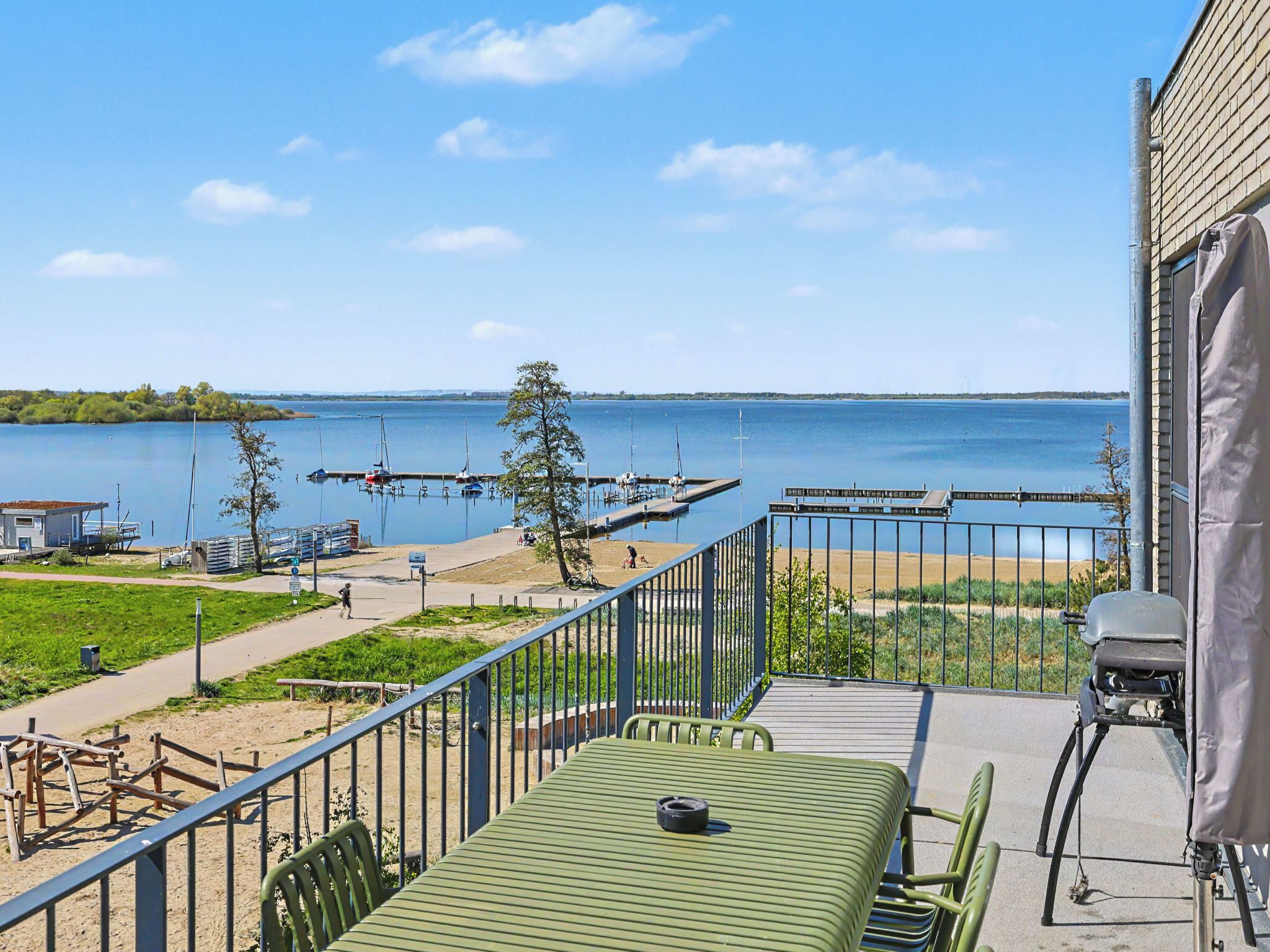 A balcony with a view of a lake, a grill, and a table with chairs.