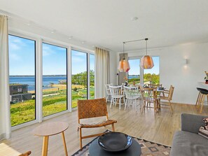 A spacious room with large windows, a dining area, and a seating area with a view of the beach.