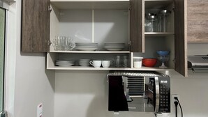 Een keuken met open kastjes, servies, glazen en een magnetron.