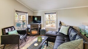 A living room with a fireplace, leather sofas, and a television. - Traverse City Cabin w/ Nearby Hiking & Lake! (Grawn)
