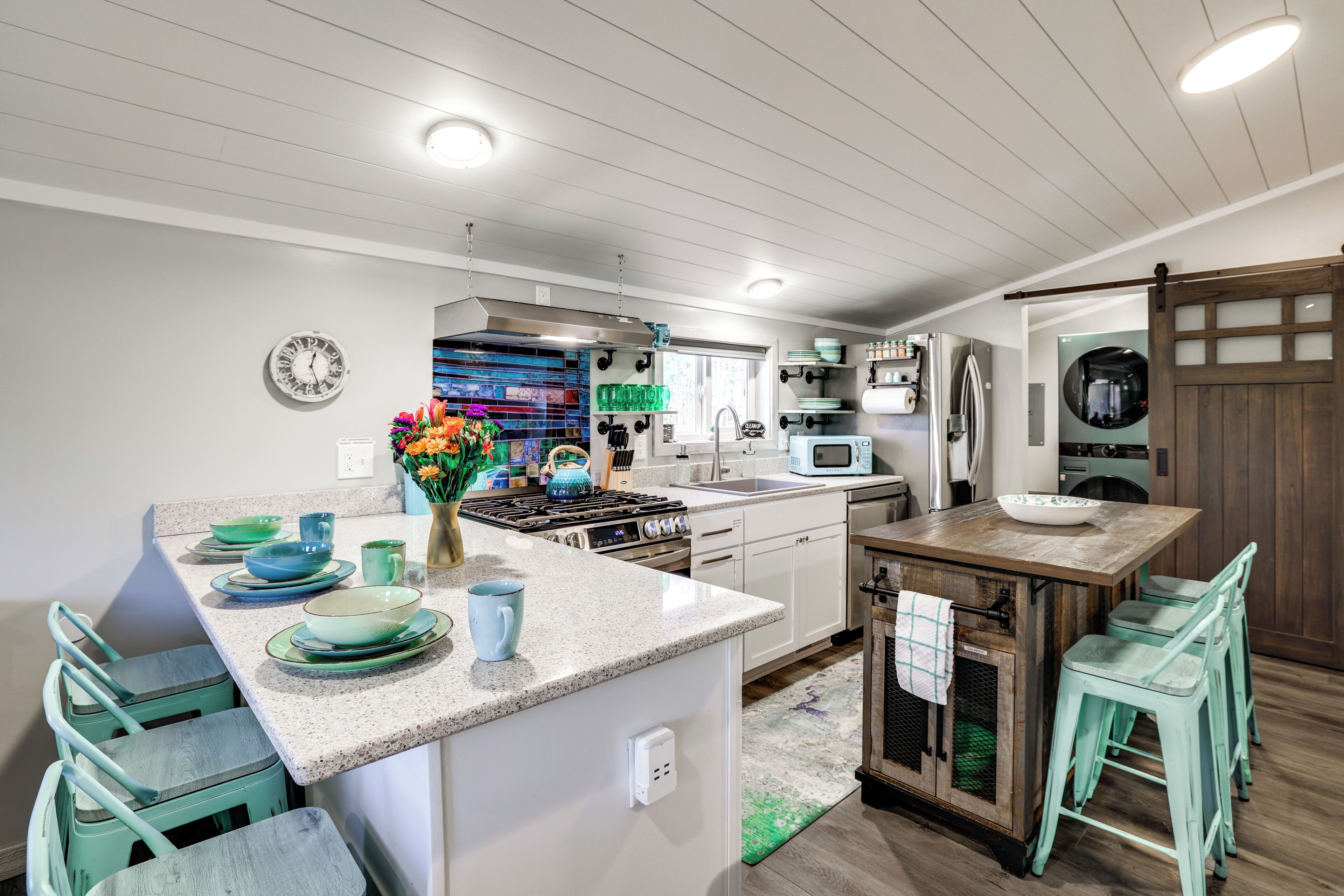 A modern kitchen with white cabinetry, a central island with stools, a stove, and a microwave.