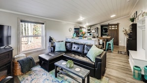 A modern living room with a black leather sofa, a coffee table, and a TV. - Traverse City Cabin w/ Nearby Hiking & Lake! (Grawn)