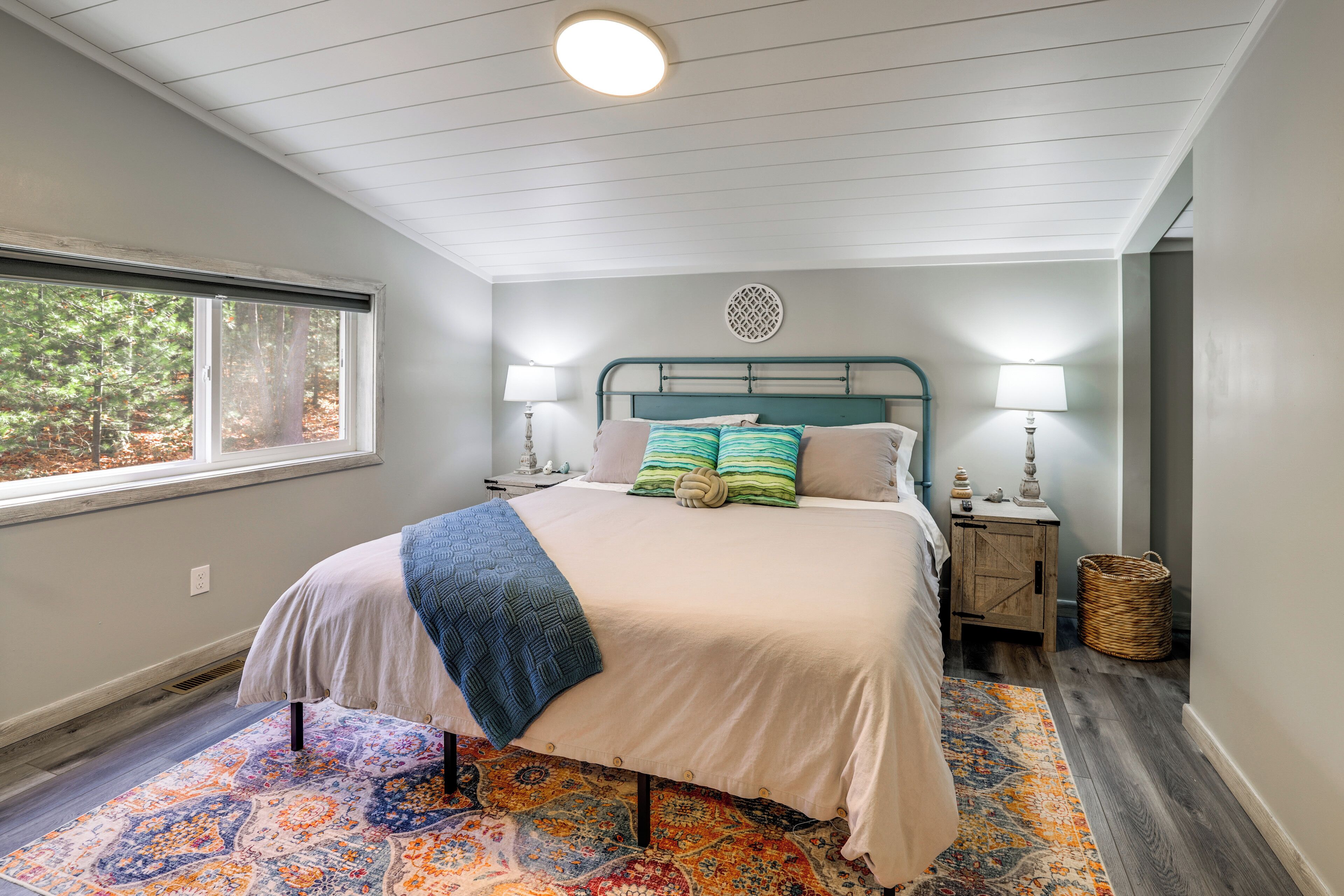 A bedroom with a bed, two bedside lamps, a window, a nightstand, and a woven basket.