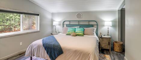 A bedroom with a bed, two bedside lamps, a window, a nightstand, and a woven basket.