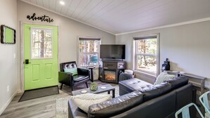 A living room with a fireplace, a television, a green door, and a sign that says 'adventure'. - Traverse City Cabin w/ Nearby Hiking & Lake! (Grawn)