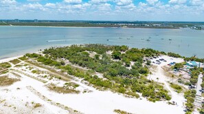 An aerial view of a coastal area with a beach, a parking lot, and a dense cluster of trees. - Waterside and Wonderful, Sunset Views, Plenty of Amenities - FMB - Condo gulf Mist - Roelens (Fort Myers Beach)