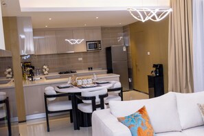Eine moderne Küche mit einer zentralen Kochinsel, einem Essbereich mit weißem Tisch und Stühlen sowie einer Wohnbereich mit einem weißen Sofa und einem farbenfrohen Kissen.