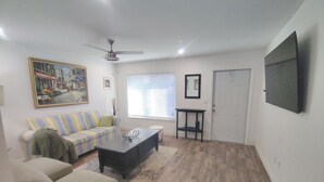 A living room with a sofa, armchair, coffee table, and a painting on the wall. - That cute house on Emerald! (Palm Bay)