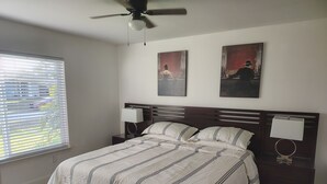 A bedroom with a bed, two wall-mounted lamps, a ceiling fan, and two framed pictures on the wall. - That cute house on Emerald! (Palm Bay)