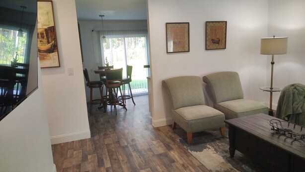 A living room with a TV, two armchairs, a coffee table, and a dining area with a table and chairs. - That cute house on Emerald! (Palm Bay)