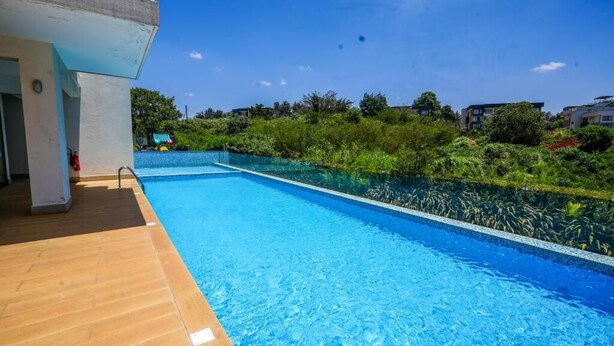 A swimming pool with a wooden deck, surrounded by lush greenery and residential buildings in the background. - 🌇 Fully Serviced 1-Bedroom Apartment at Riverbank, Two Rivers – Nairobi (Nairobi)