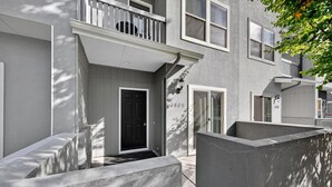 Un moderno edificio de apartamentos con puerta negra, barandillas blancas y una barrera de hormigón.