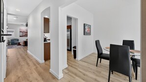 Un interior moderno con zona de comedor que incluye una mesa redonda y sillas negras, cocina equipada con refrigerador, y sala de estar con sofá y una mesita de centro.