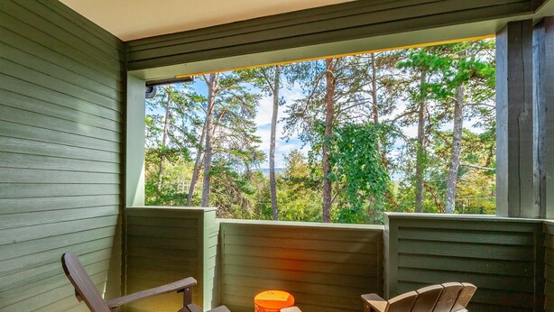 A wooden deck with two Adirondack chairs and a small orange stool, overlooking a forested area through a window. - Bespoke Outpost: A stylish 3-bedroom retreat in scenic Chattanooga, TN. (Chattanooga)