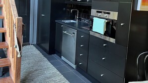 Une cuisine de taille réduite avec des meubles de couleur sombre, une cuisinière en acier inoxydable et un escalier en bois.