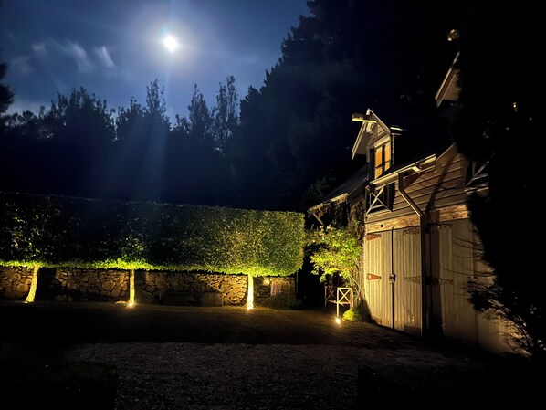 Un granero rústico con pared de piedra y cerca de madera, iluminado por una luz tenue.