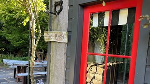 Une porte rouge avec une enseigne indiquant « The Barn », et un mur de pierres visible à travers la fenêtre.