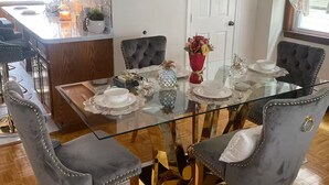 A dining area with a glass table, grey upholstered chairs, and a red vase with flowers. - Lorenzo Inn (Boston)